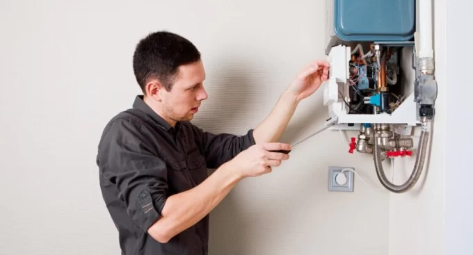 Technician inspecting and repairing a home heating unit using a screwdriver.